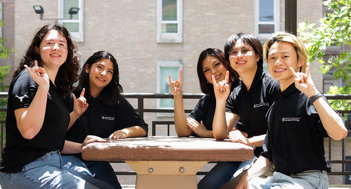 Five UT Resident Assistants sit in the Jester Plaza while making the Hook ‘em hand sign
