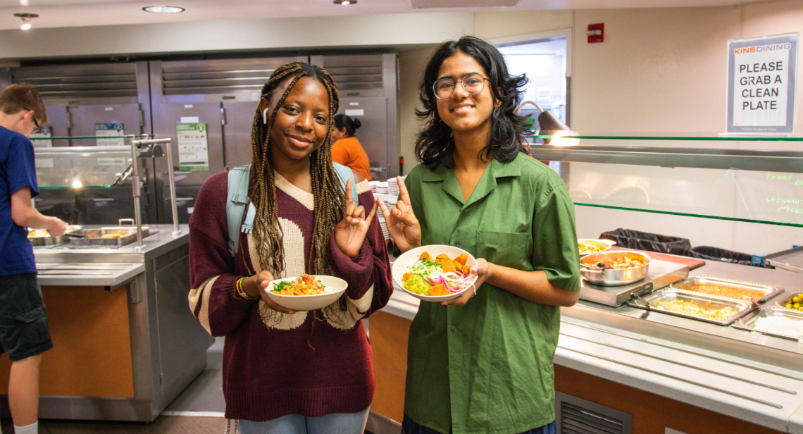 Two students posing with a Hook ‘em hand sign inside of Kins Dining