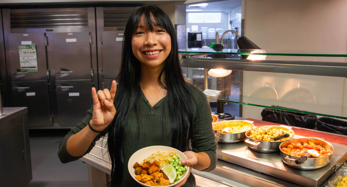 Student posing with a Hook ‘em hand sign inside of Kins Dining