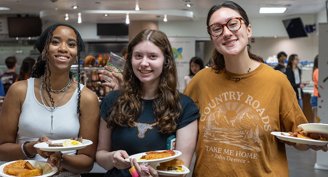 Three students posing with their late night breakfast platters at Kins Dining