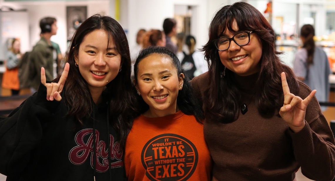 Three students smile in a dining hall at the University of Texas