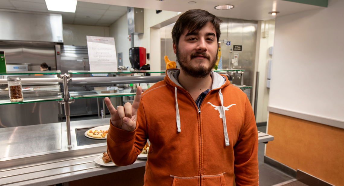 Hallo-wings Event Student inside of Kins Dining posing with a hook ‘em hand sign