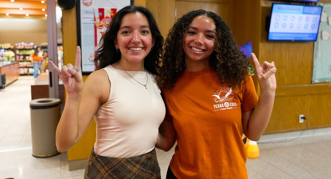 Two UT students make the Hook ‘Em hand sign outside Kin’s Market.