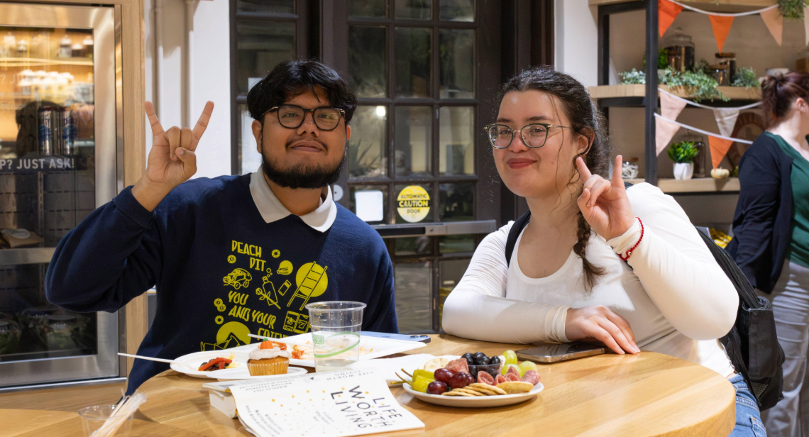 Two students dining in at Littlefield Patio  Café posing with a hook ‘em hand sign. 
