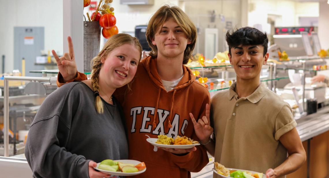 Sun Noodle Station Takeover Three students dining in at Kins Dining posing with a hook ‘em hand sign.