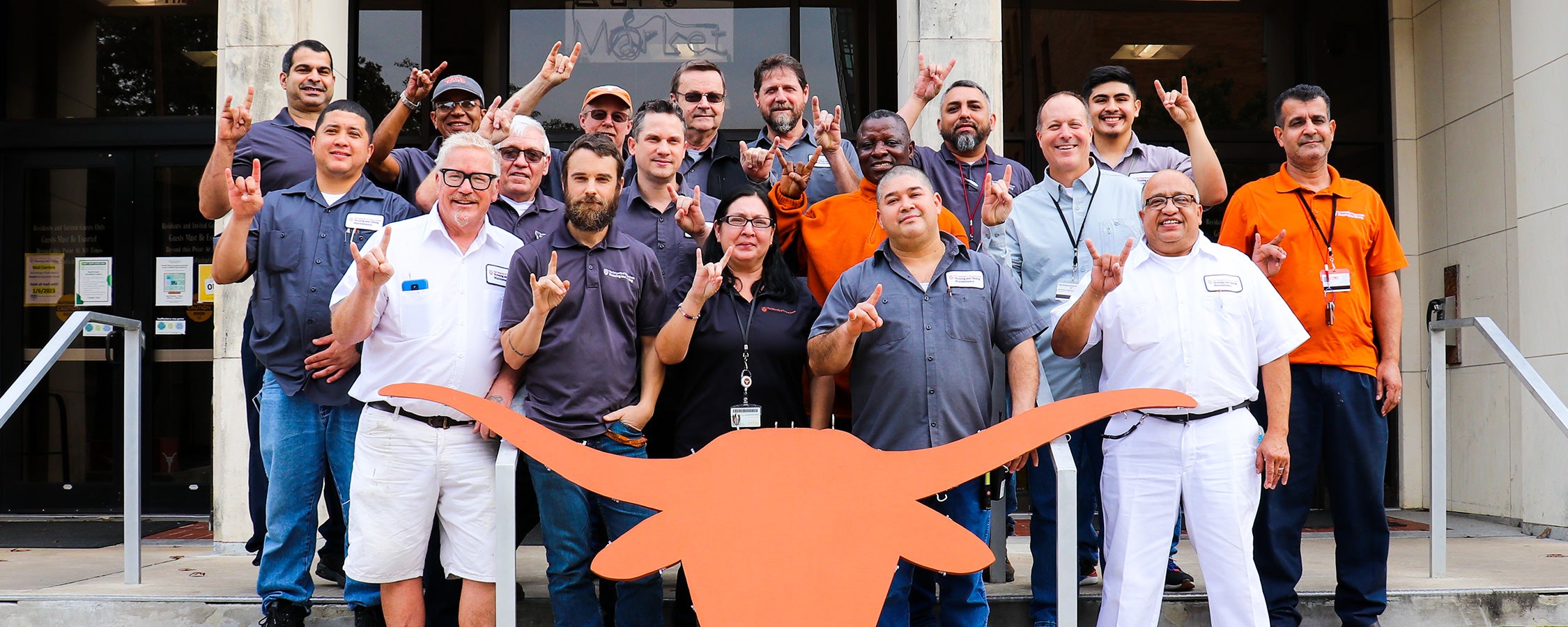 A group of UT staff members pose together while making the Hook ‘em hand sign behind a Longhorn silhouette