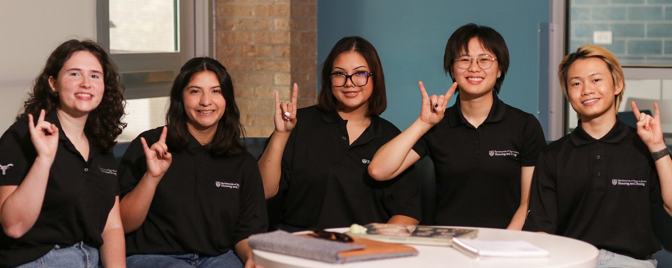 Five UT resident assistants pose while making the Hook ‘em hand sign in the Jester Fireplace Lounge