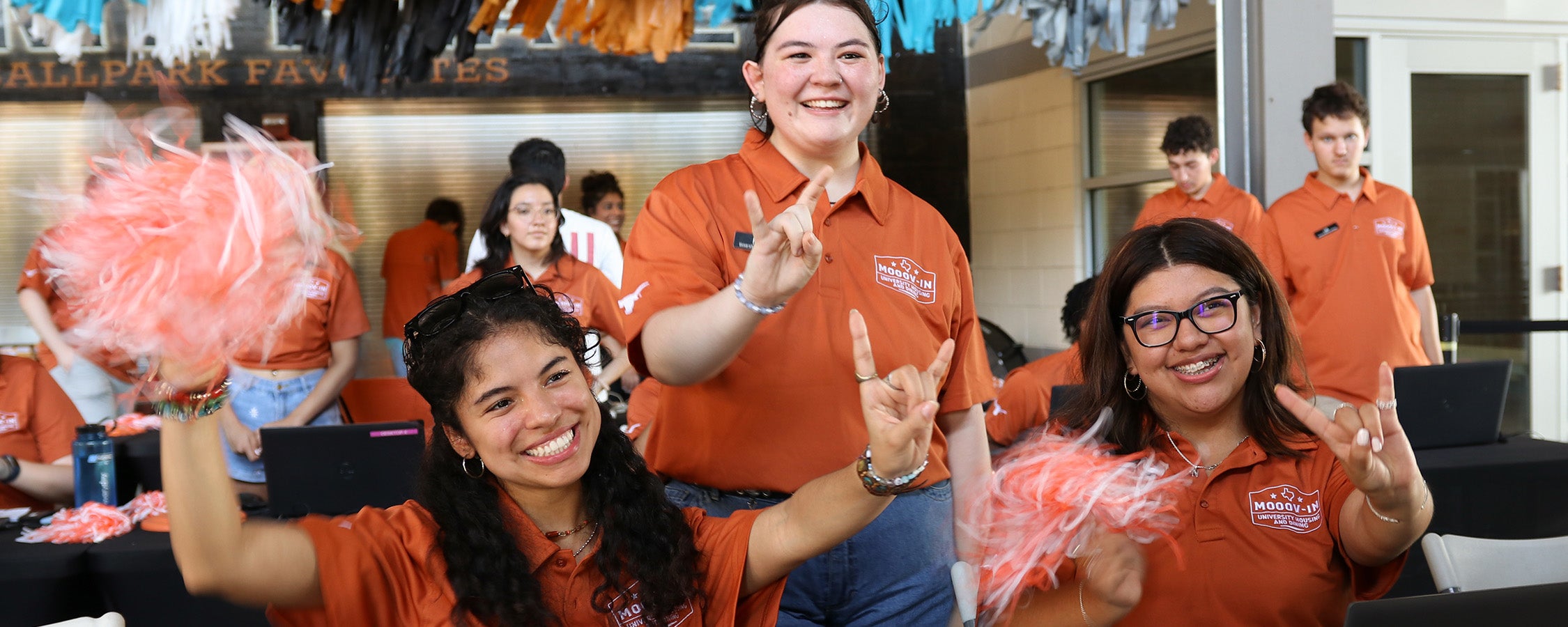 Three UT student staff members make the Hook ‘em hand sign while working a check-in table at Disch-Falk Field during Mooov-In
