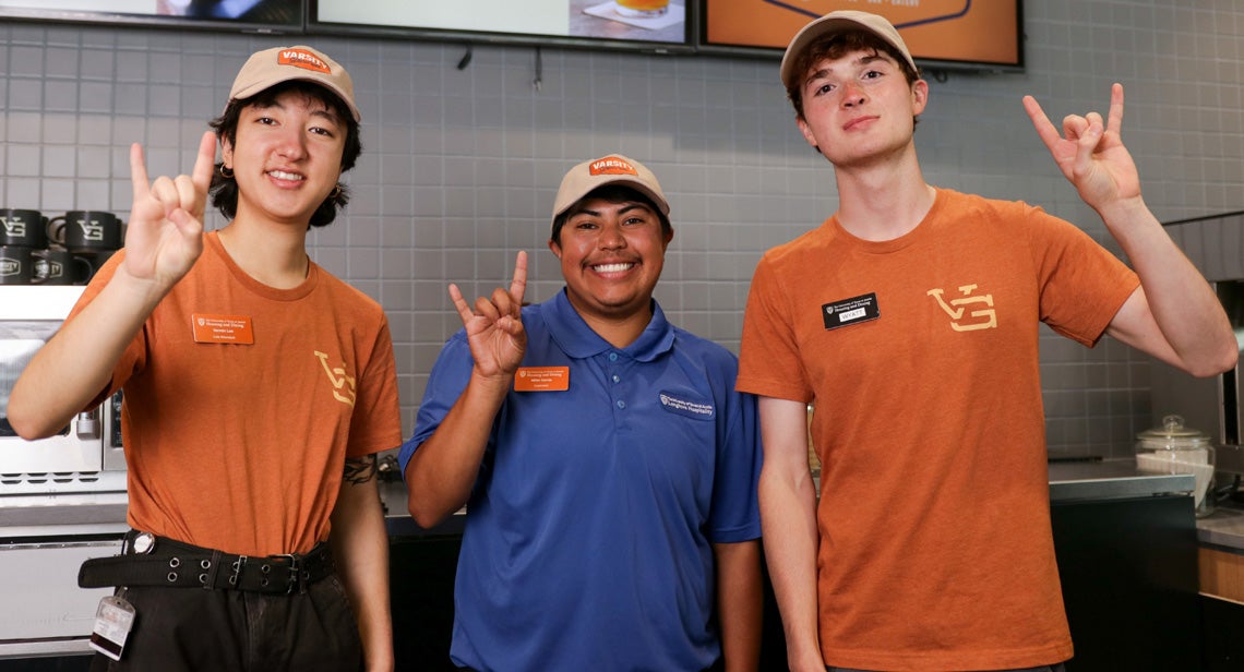 Three UT student staff members pose while making the Hook ‘Em hand sign in Varsity Grounds