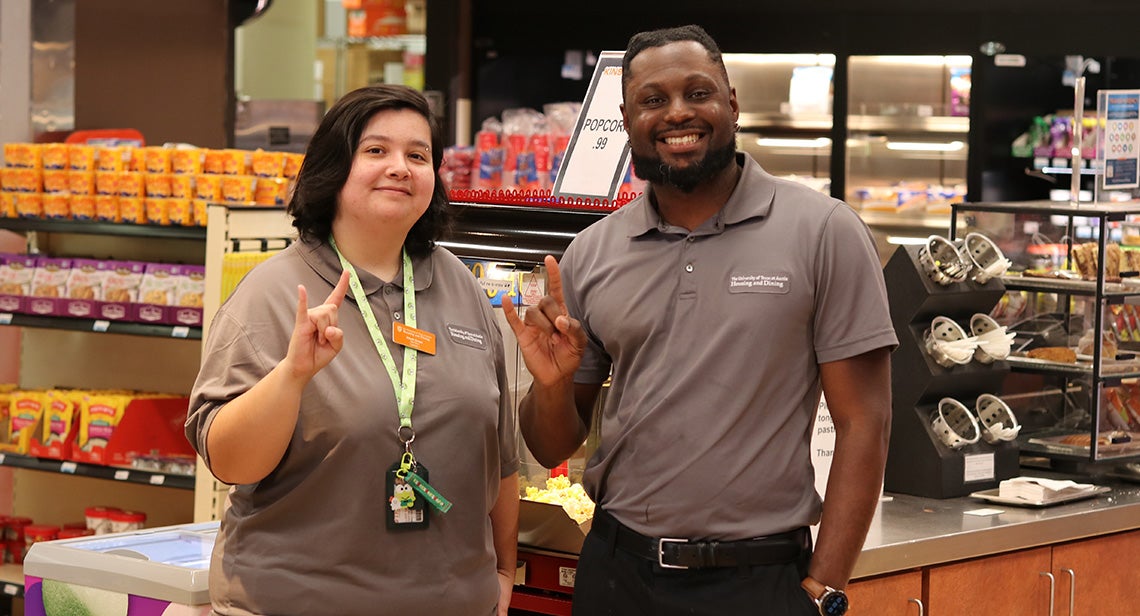 Two UT staff members pose while making the Hook ‘Em hand sign in Kins Market