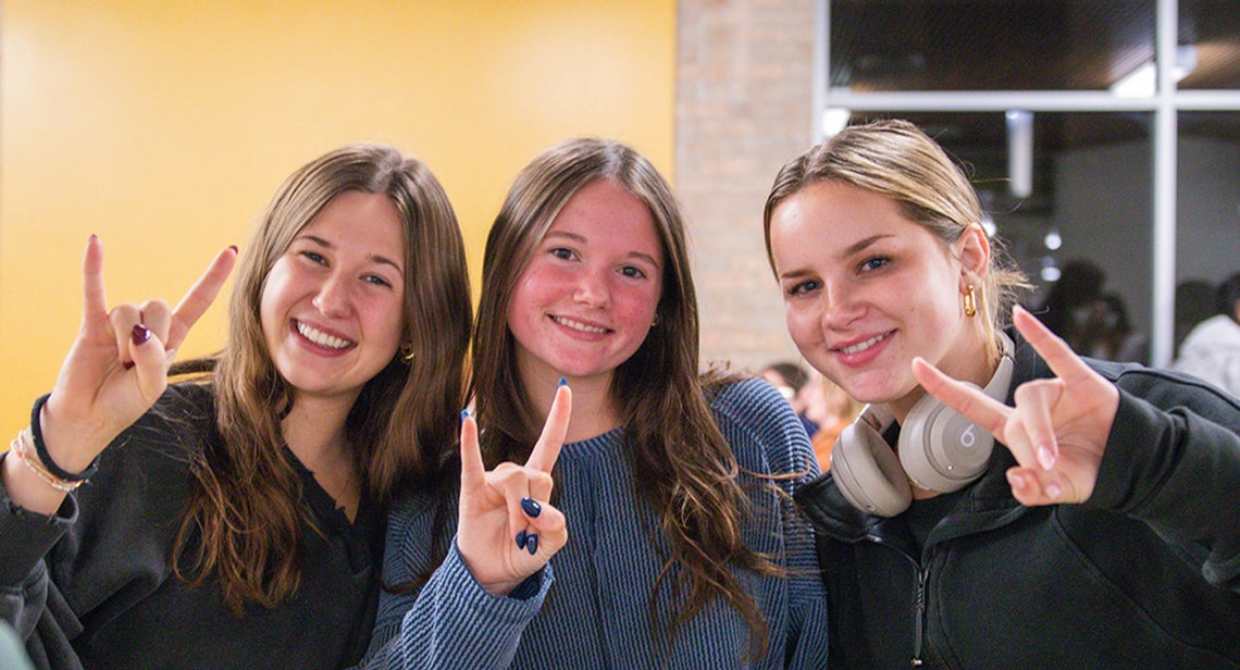 Three UT students pose together while making the Hook ‘Em hand sign