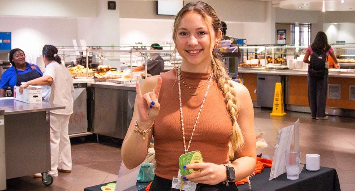 A UT student poses while holding a plate of food and making the Hook ‘Em hand sign