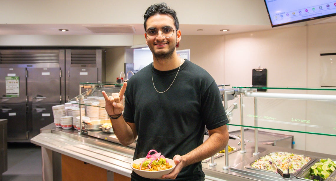 A UT student poses while holding a plate of food and making the Hook ‘Em hand sign