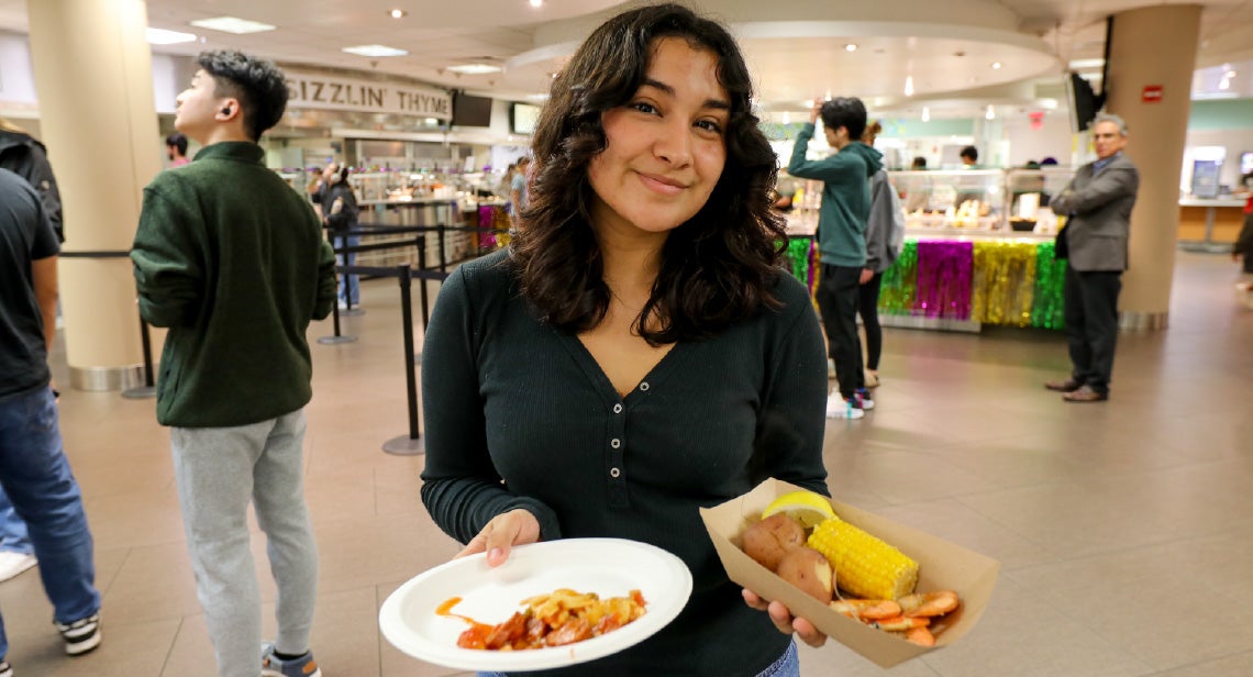 A UT student poses while holding two plates of food in Kins Dining