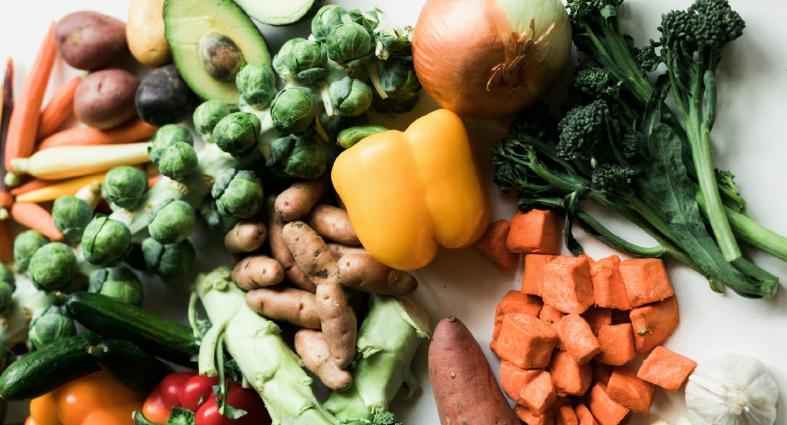 An assortment of vegetables including potatoes, carrots, bell pepper, broccoli, brussels sprouts and onions.
