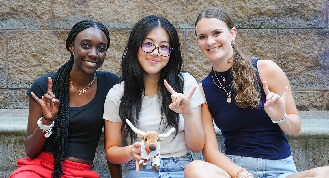 Three UT students pose together with a Bevo plush while making the Hook ‘em hand sign. 