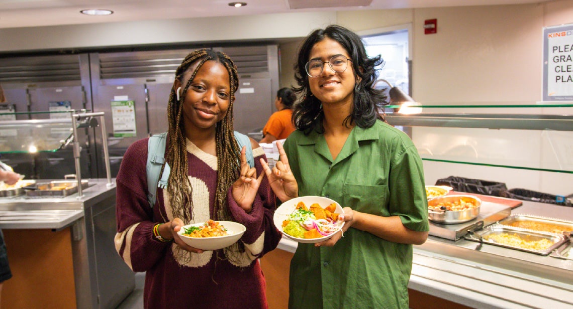 Two UT students pose while making the Hook ‘Em hand sign and holding plates of food