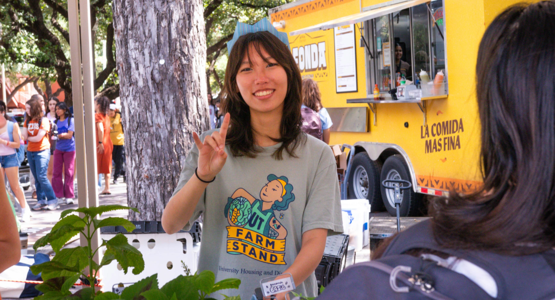 UT Farm Stand student employee posing with a hook ‘em hand sign
