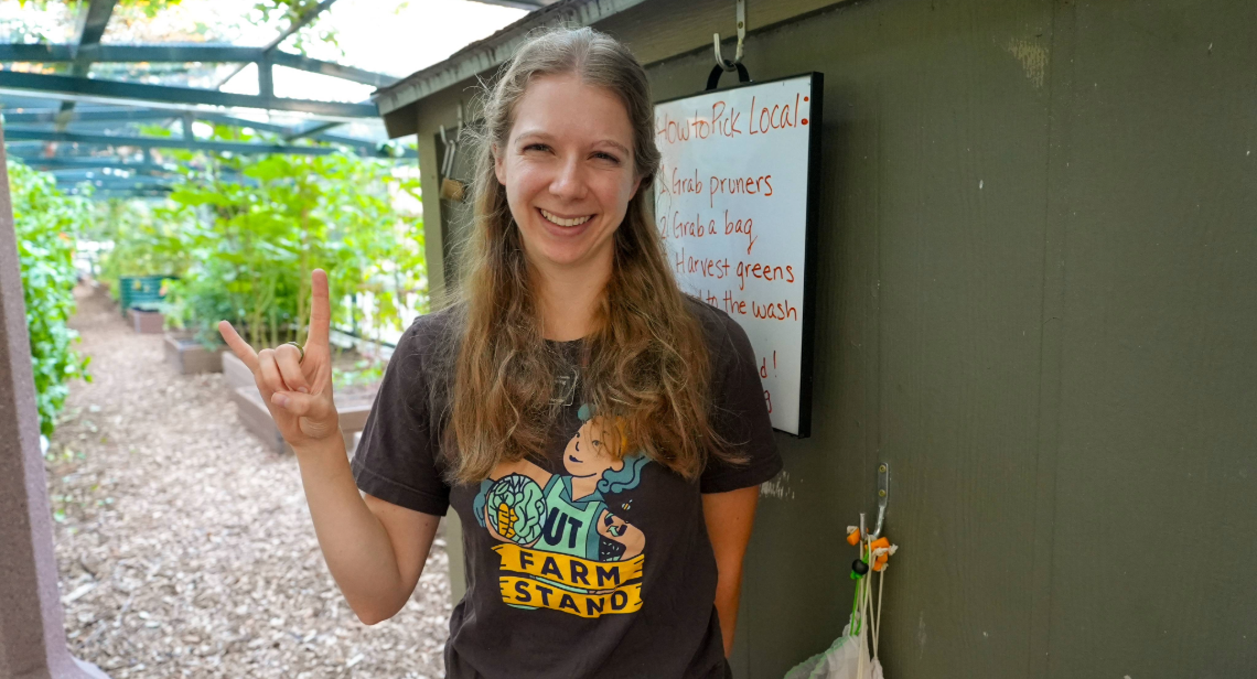 UT Farm Stand student employee posing with a hook ‘em hand sign at the Jester Gardens