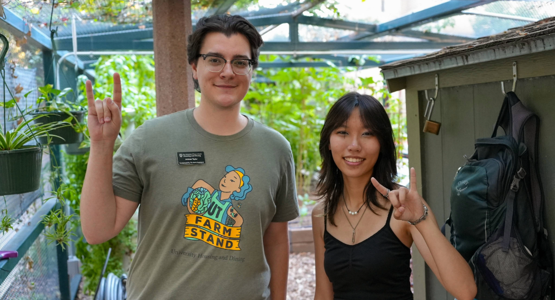 Two UT Farm Stand student employees posing with a hook ‘em hand sign at the Jester Gardens
