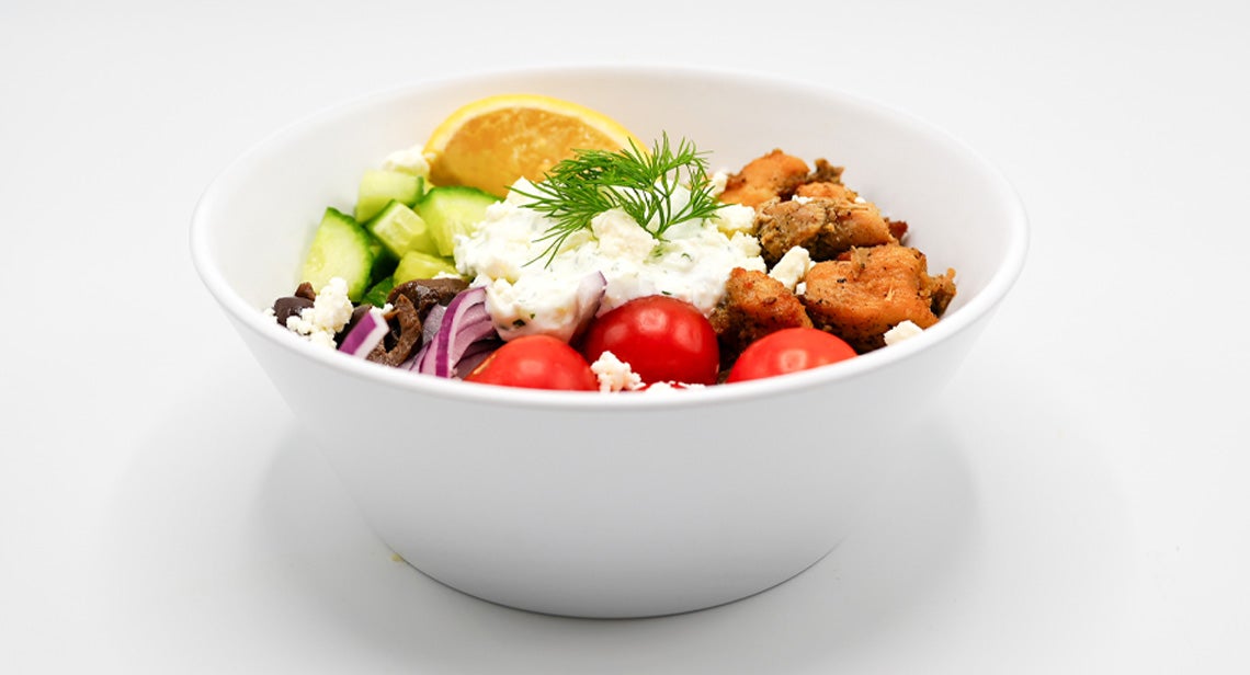 A Mediterranean bowl with vegetables, tzatziki sauce, feta cheese and other toppings