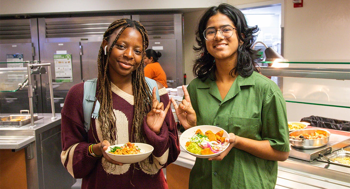 Two UT students pose together while holding plates and making the Hook ‘em hand sign