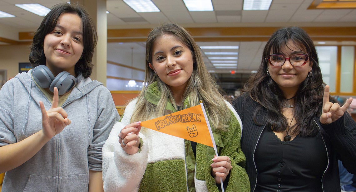 Three UT students pose together while making the Hook ‘Em hand sign.