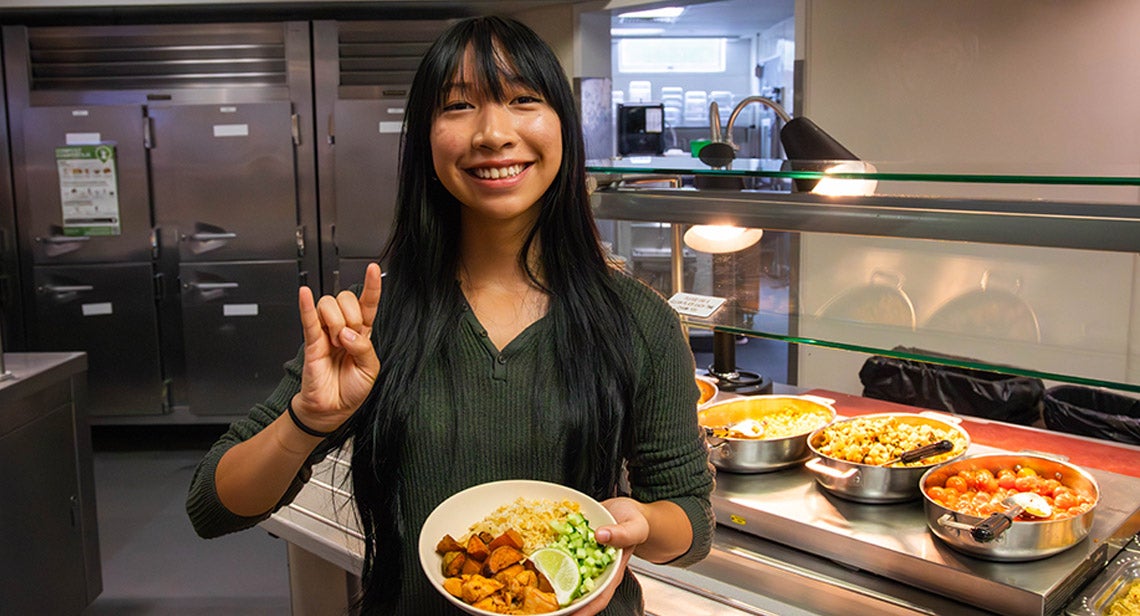 A UT student poses while making the Hook ‘Em hand sign while holding a plate of food.