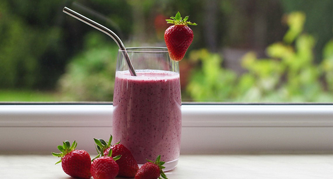 A smoothie with a straw and strawberries next to it.