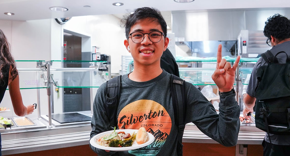 UT student posing with a hook ‘em hand sign at Kins Dining