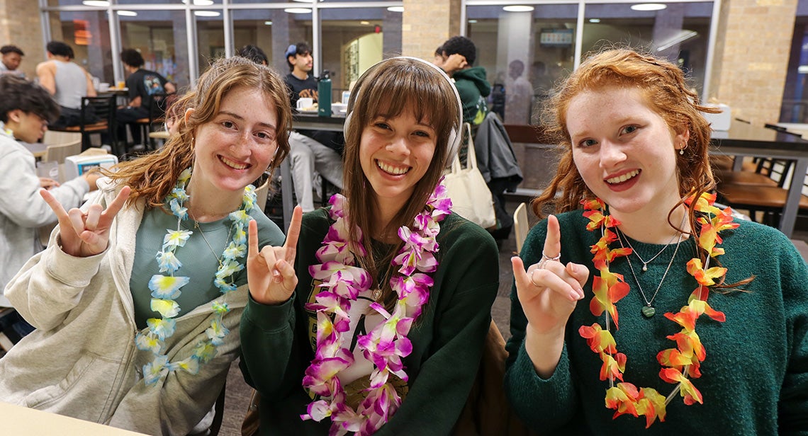 Three UT students pose together while making the Hook ‘Em hand sign at a Luau Night event in J2 Dining
