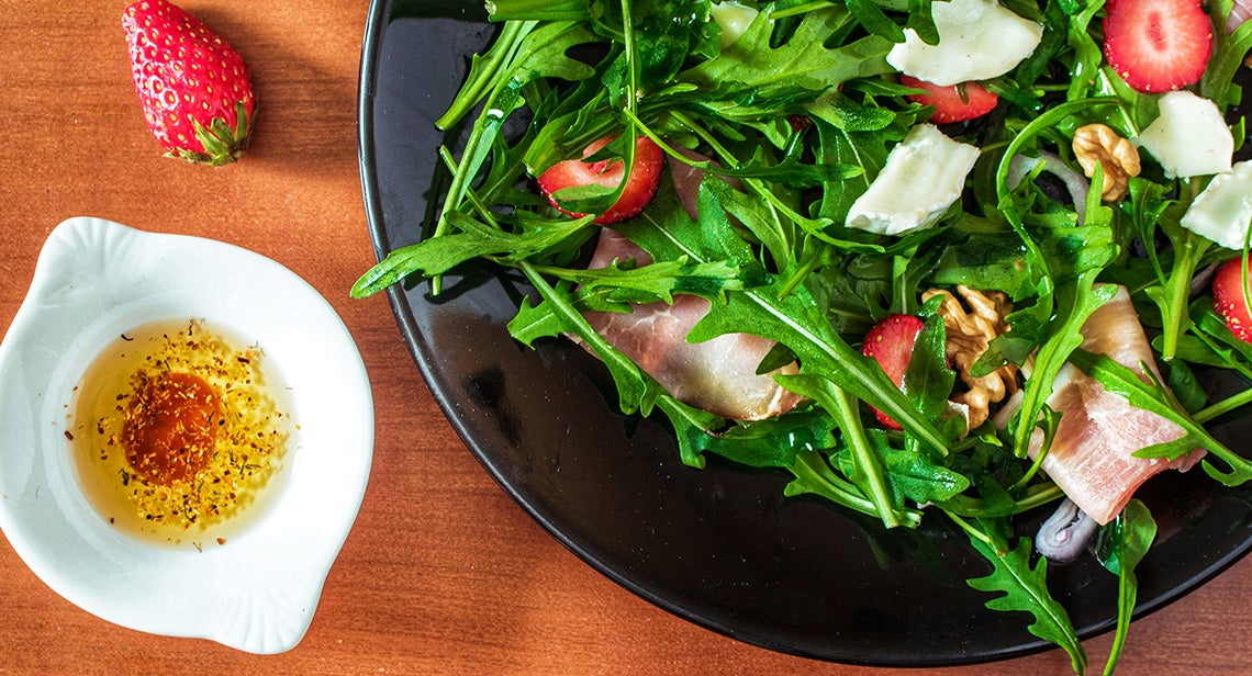 A salad with strawberries and a side of vinaigrette