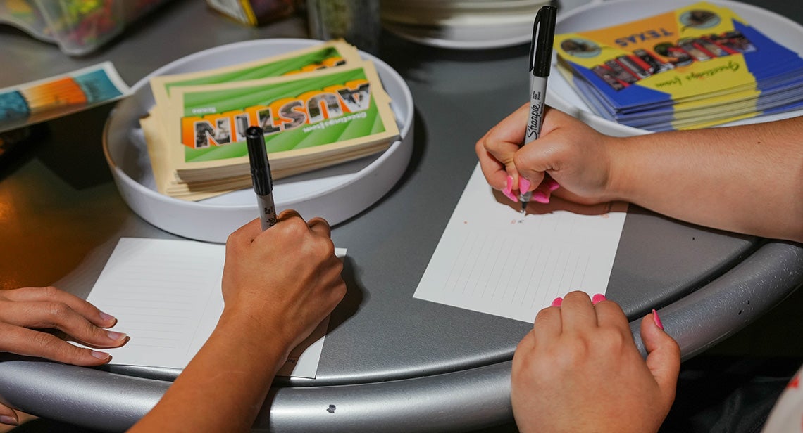Two UT students write on “Welcome to Austin” postcards