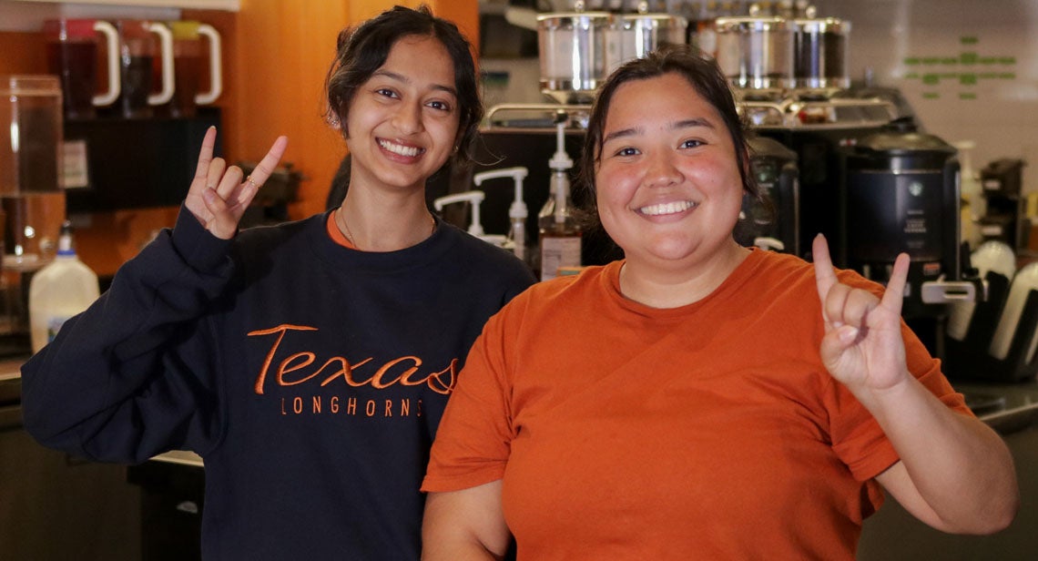 Two UT student staff members make the Hook ‘em hand sign at Jester Java