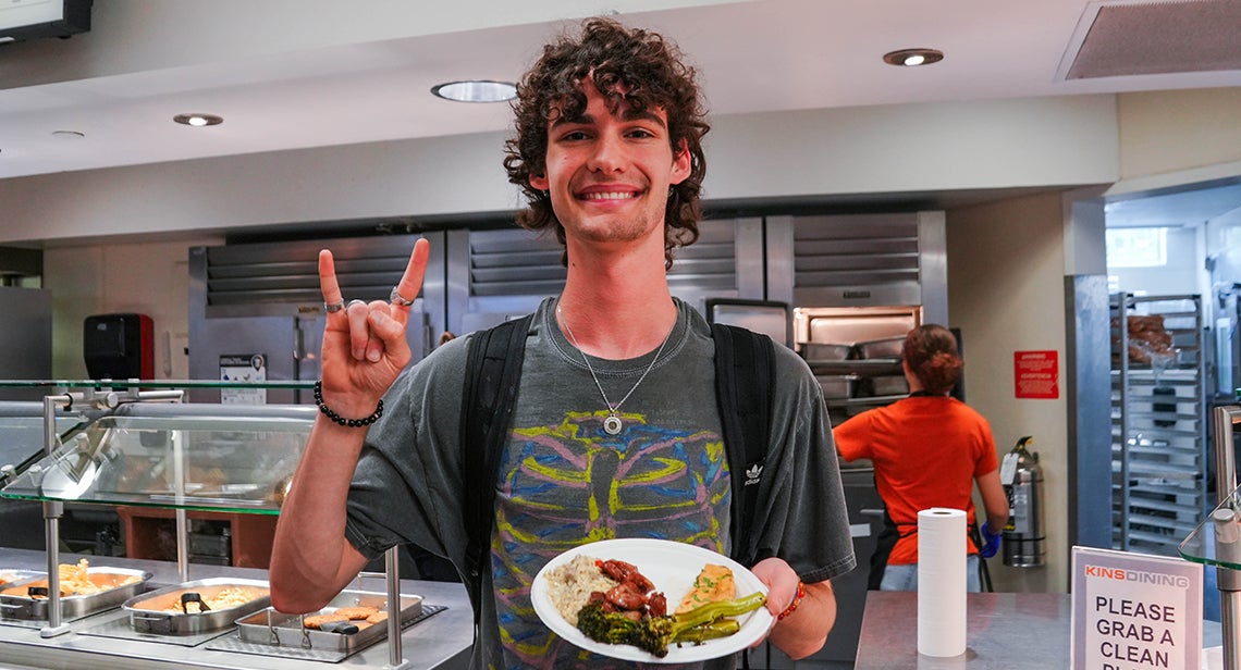 A UT student makes the Hook ‘em hand sign while holding a plate in Kins Dining. 