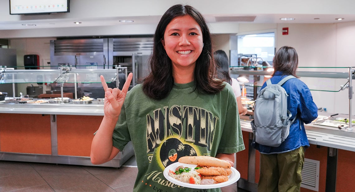 A UT student makes the Hook ‘em hand sign while holding a plate in Kins Dining.