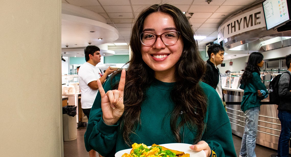 A UT student makes the hook ‘em hand sign while holding a plate of food in Kins Dining. 