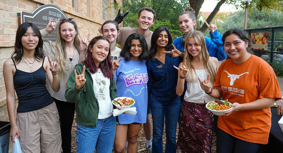 A group of UT students pose together in the Jester Gardens while making the Hook ‘em hand sign and holding bowls of salad. 