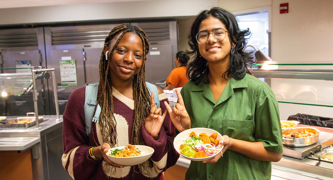 Two UT students pose together while making the Hook ‘Em hand sign and holding dishes.