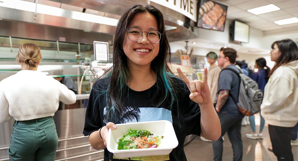 A UT student holds a salad bowl and makes the Hook ‘em hand sign in J2 Dining. 