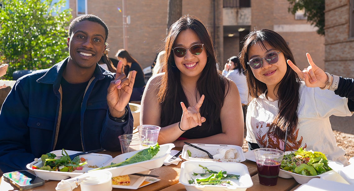 Three UT students pose together while making the Hook ‘Em hand sign at the Pick Local event outside San Jacinto Hall.