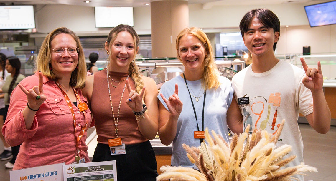 Three UHD registered dietitians pose together while making the Hook ‘em hand sign in Kins Dining. 