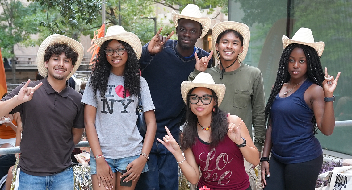 A group of UT students in western-style hats pose together while making the Hook ‘Em hand sign at Jester Plaza during the Texas Block Party Event