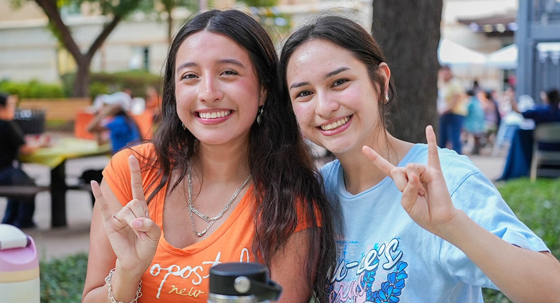 Two UT students pose together while making the Hook ’em hand sign in front of Jester Corner