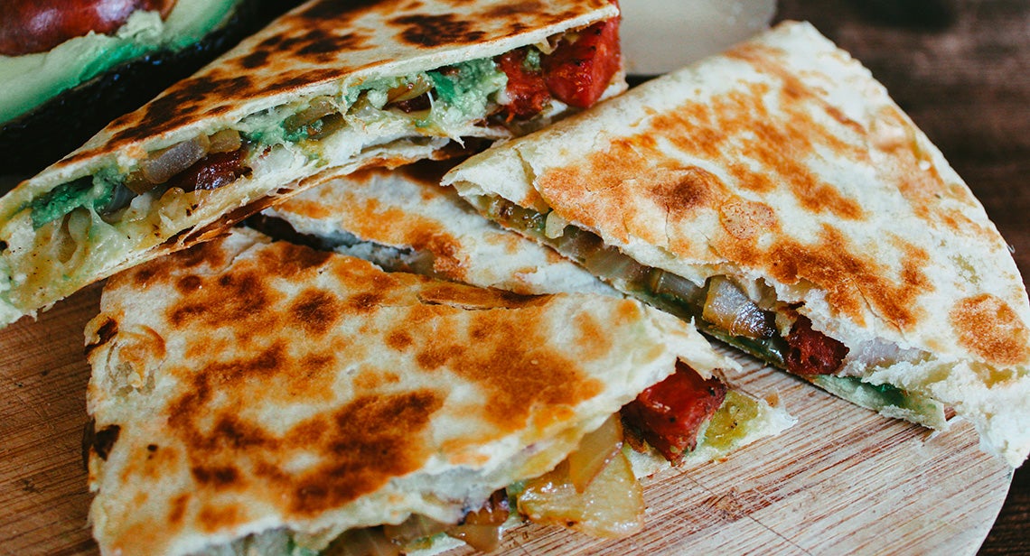 A close up of a quesadilla featuring onions, avocado and green chile