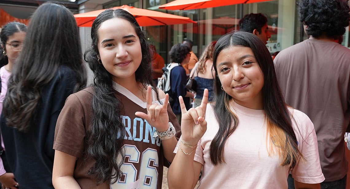 Two UT students pose together while making the Hook ’em hand sign at the Texas Block Party in front of Jester Corner