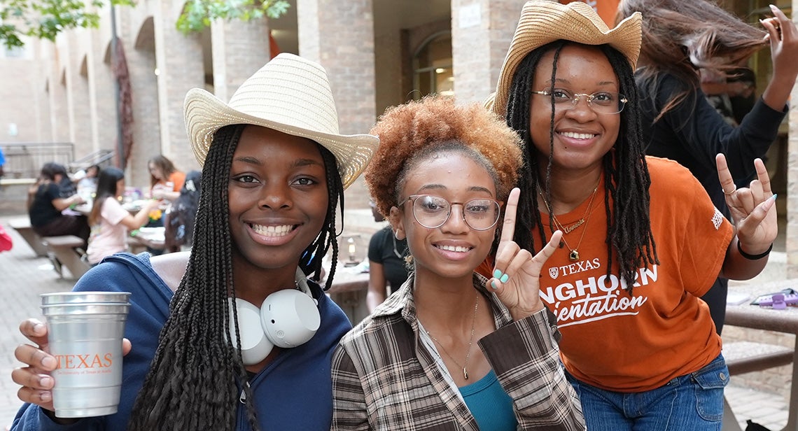 Three UT students pose together while making the Hook ’em hand sign at the Texas Block Party in front of Jester Corner