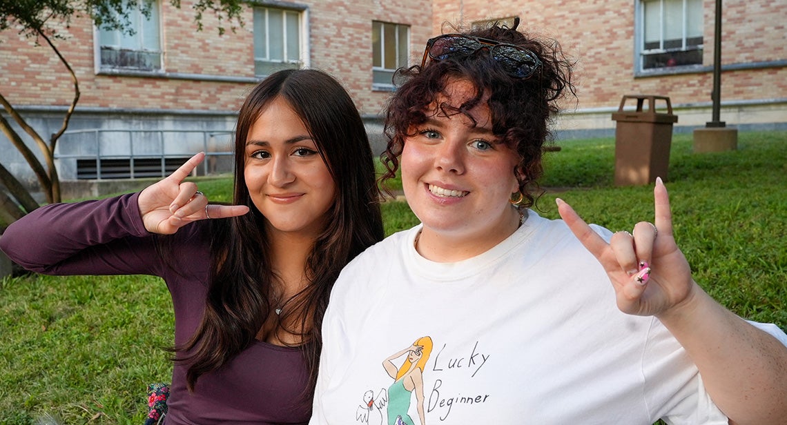 Two UT students pose together while making the Hook ’em hand sign at the Texas Block Party in front of Jester Corner