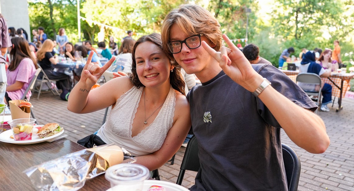 : Two UT students pose together while making the Hook ‘em hand sign at a UHD event