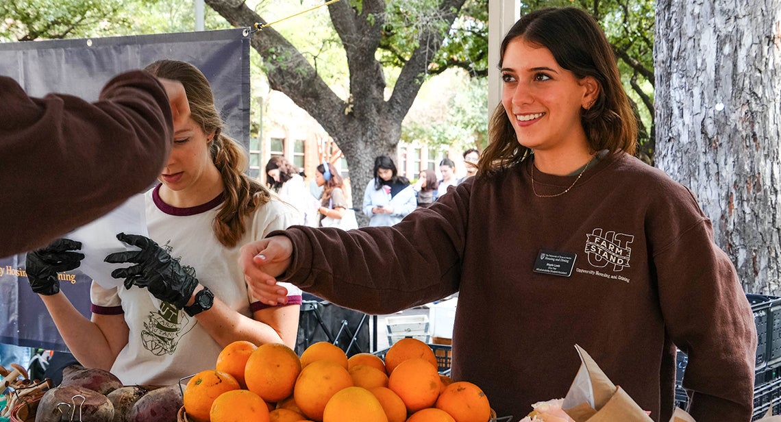 A UT student smiles while handing over produce at a UT Farm Stand market